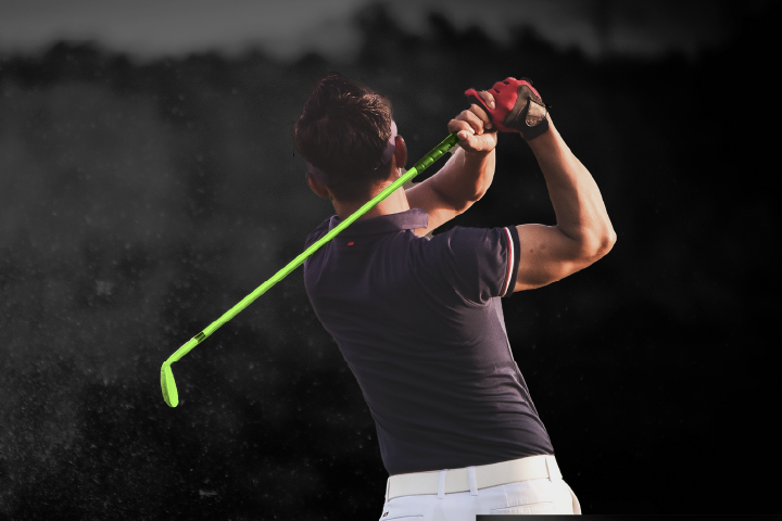 A person swinging a golf club. The golf club is in the motion of a swing and the club is green. They also wearing a red glove on their right hand.