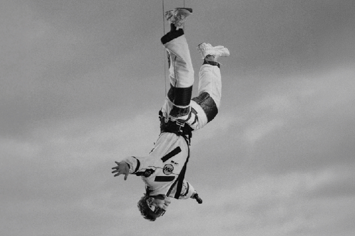 Singer Robbie Williams hanging upside-down wearing a skydiving jumpsuit.